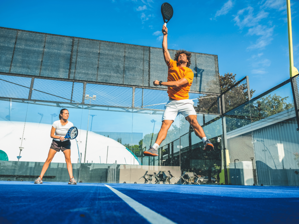 Padel player jumping to hit ball on blue court