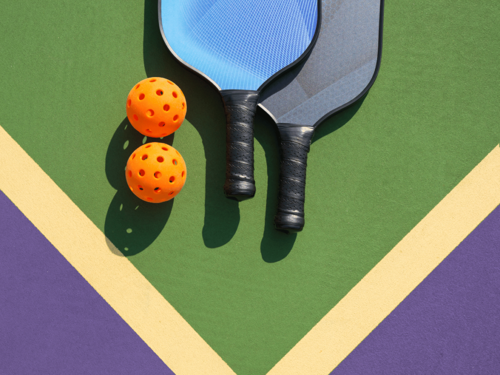 Top view of two pickleball rackets and two balls on corner of green court